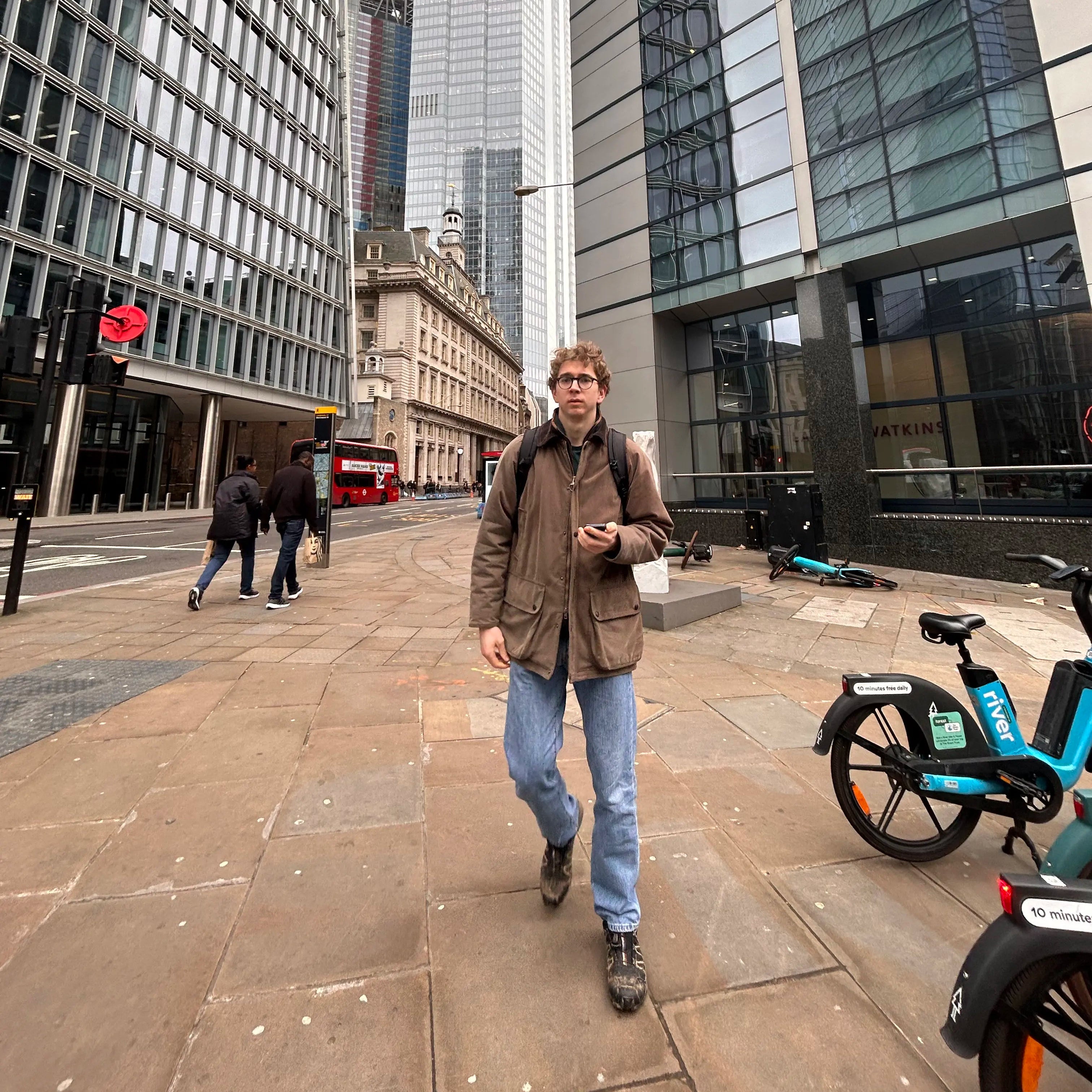 Man walking in london with brown coat and blue jeans on.