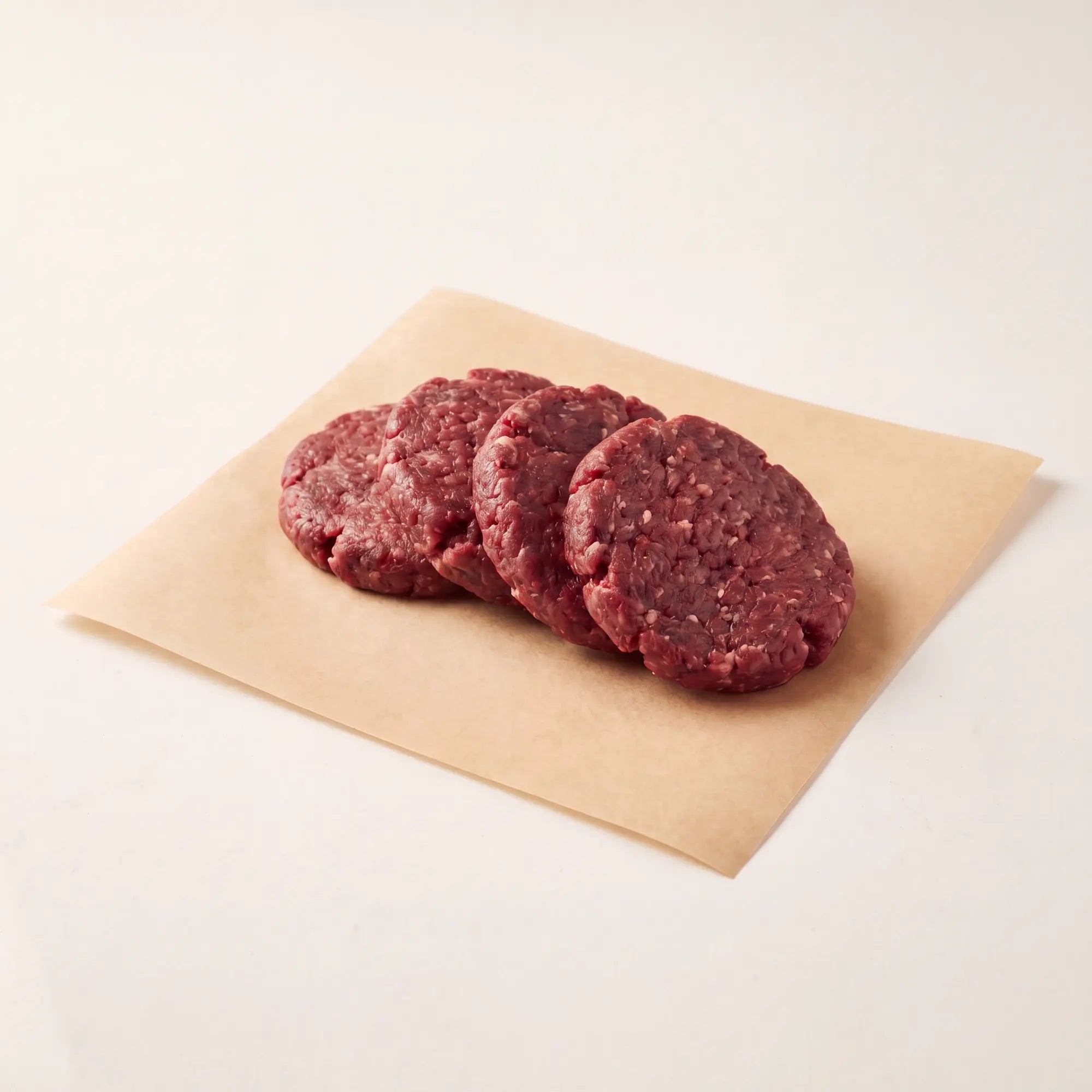 Four raw venison burger patties on a piece of brown paper with a white background