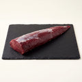 Raw venison loin / saddle on a black slate surface with a white background