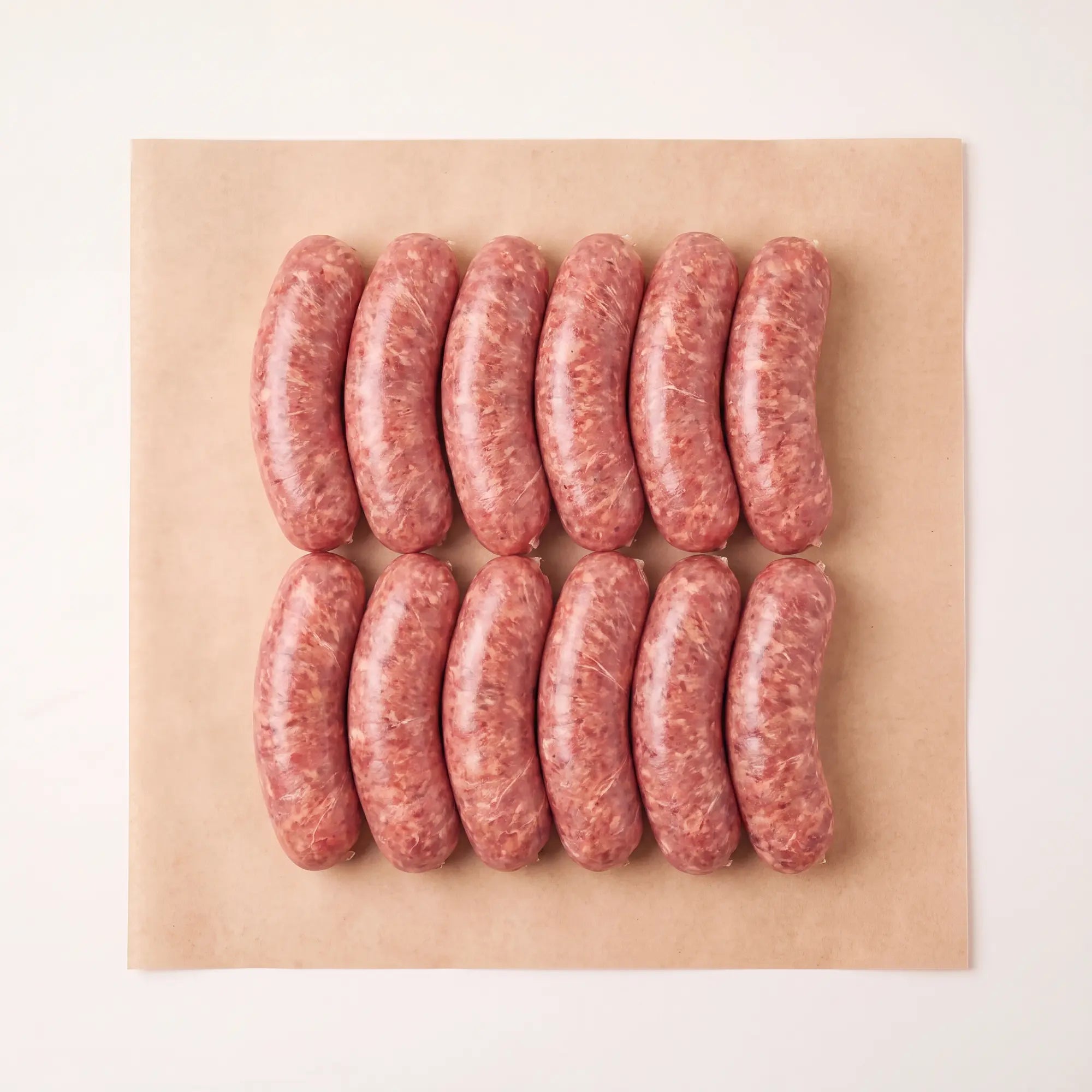 Twelve raw venison sausages arranged in two rows on a square sheet of brown parchment paper, photographed from above against a clean white background.