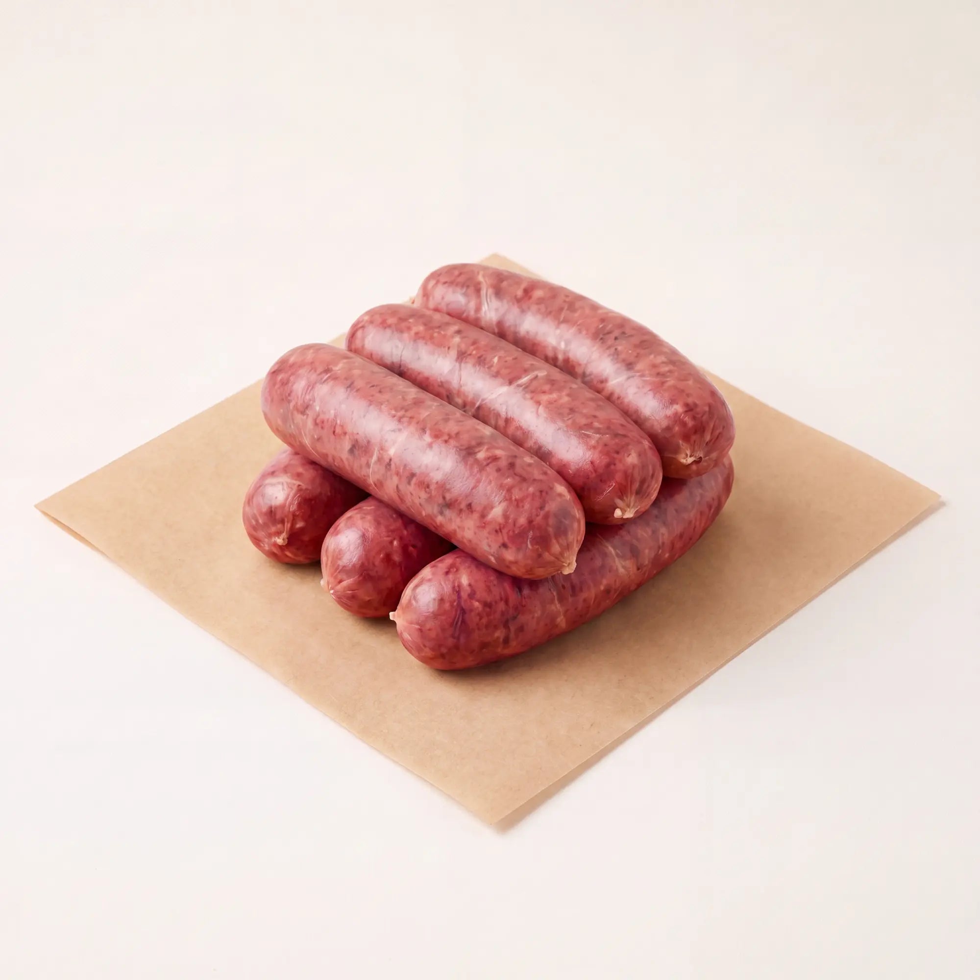 Six raw venison sausages on a piece of brown paper with a white background
