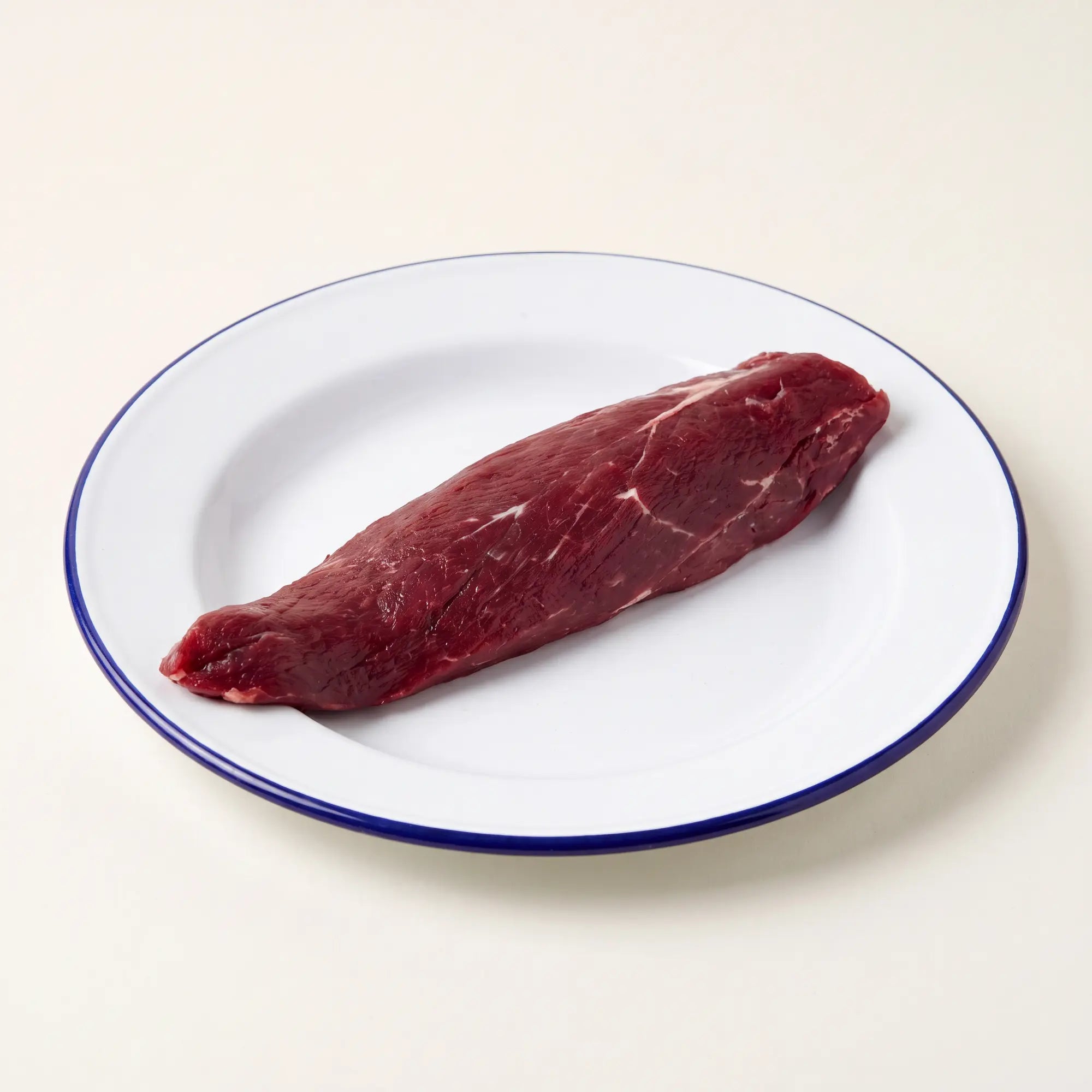 Venison tenderloin on small white with blue rim plate with a beige background